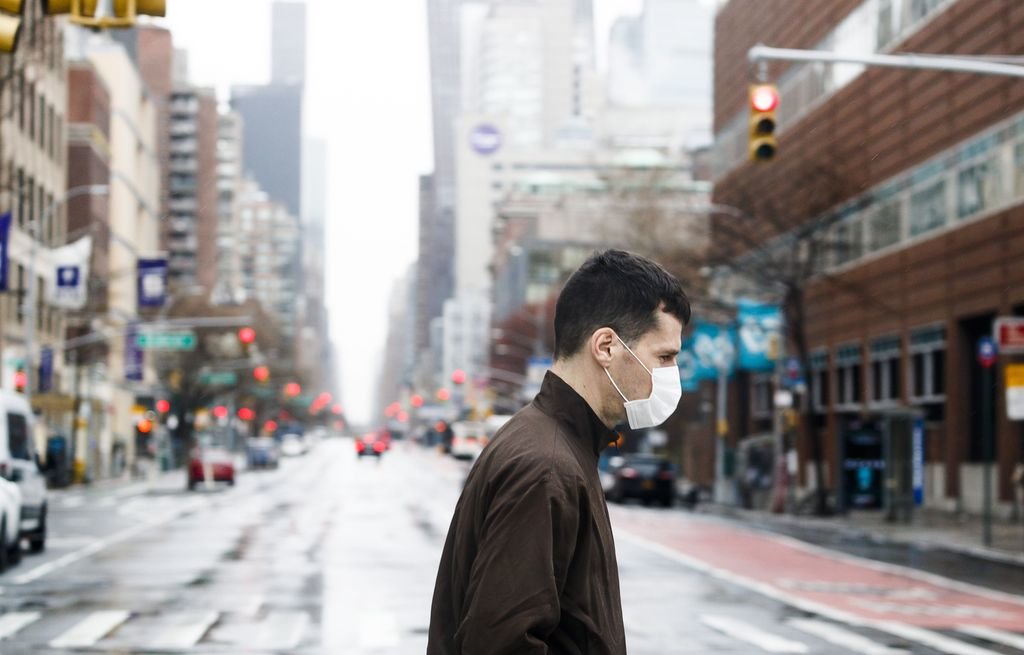 Un  hombre protegido con una máscara cruza por una casi deierta avenida de Nueva York.