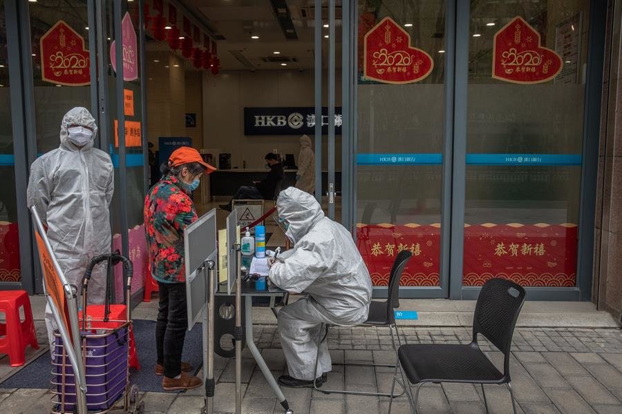 Un trabajador en un equipo de protección (R) registra la información de una anciana en la entrada de un banco en Wuhan, China
