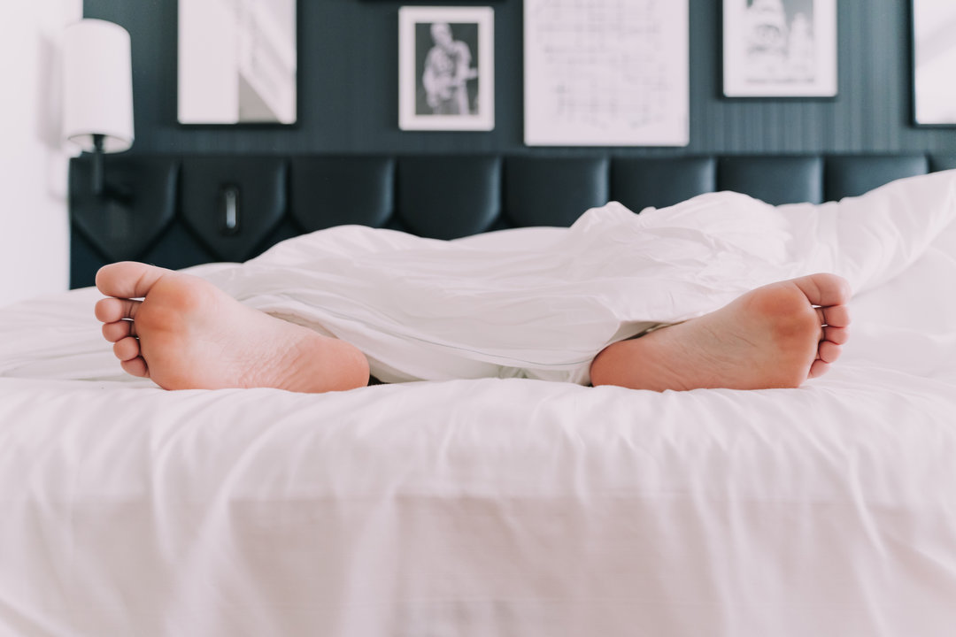 Una persona mantiene los pies fuera de las sábanas, durante sus horas de sueño.