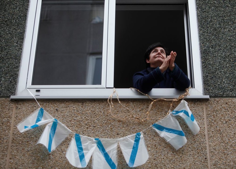 Una vecina de Arteixo, con su ventana engalanada de banderas gallegas, aplaude a los sanitarios.