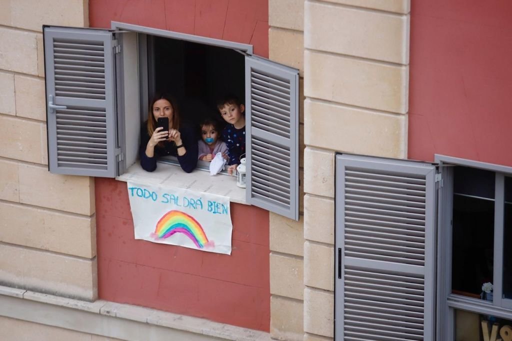 Dos niños con su madre mandan ánimos desde un balcón.