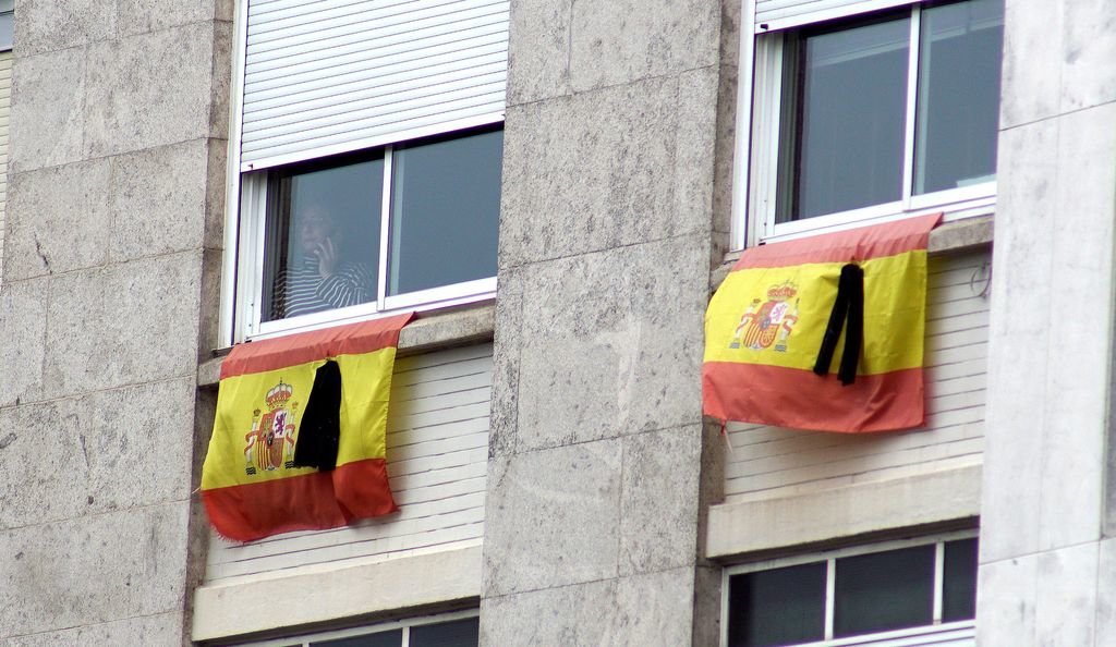 Banderas de España con crespones negros en señal de luto por los miles de fallecidos cuelgan de las ventanas de una vivienda de Vigo.