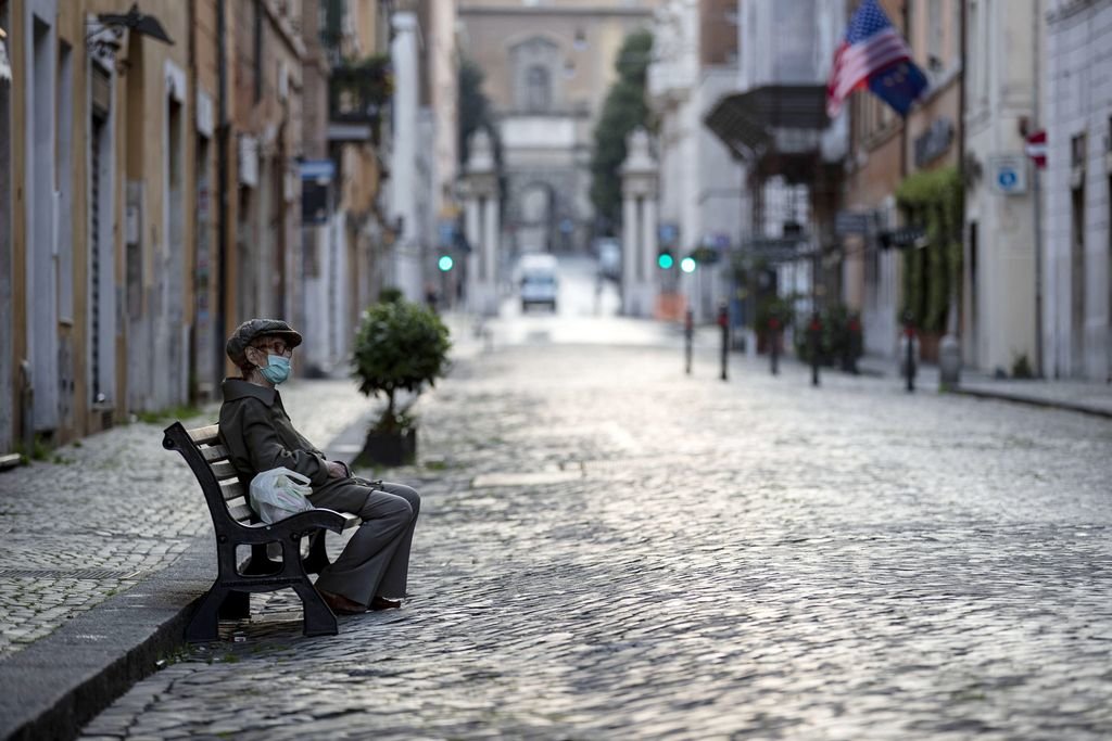 Un hombre descansa en un banco en una desierta calle de Roma.