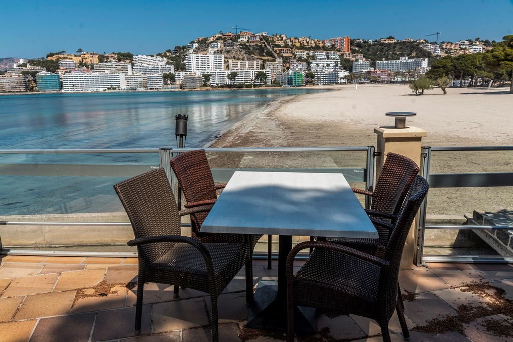 Terraza de un restaurante cerrado con vistas a la playa de Santa Ponça, también vacía de público.