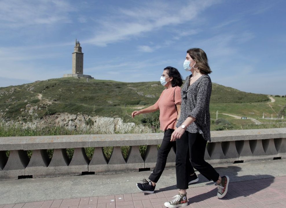 Dos mujeres pasean por A Coruña, con la Torre de Hércules al fondo.