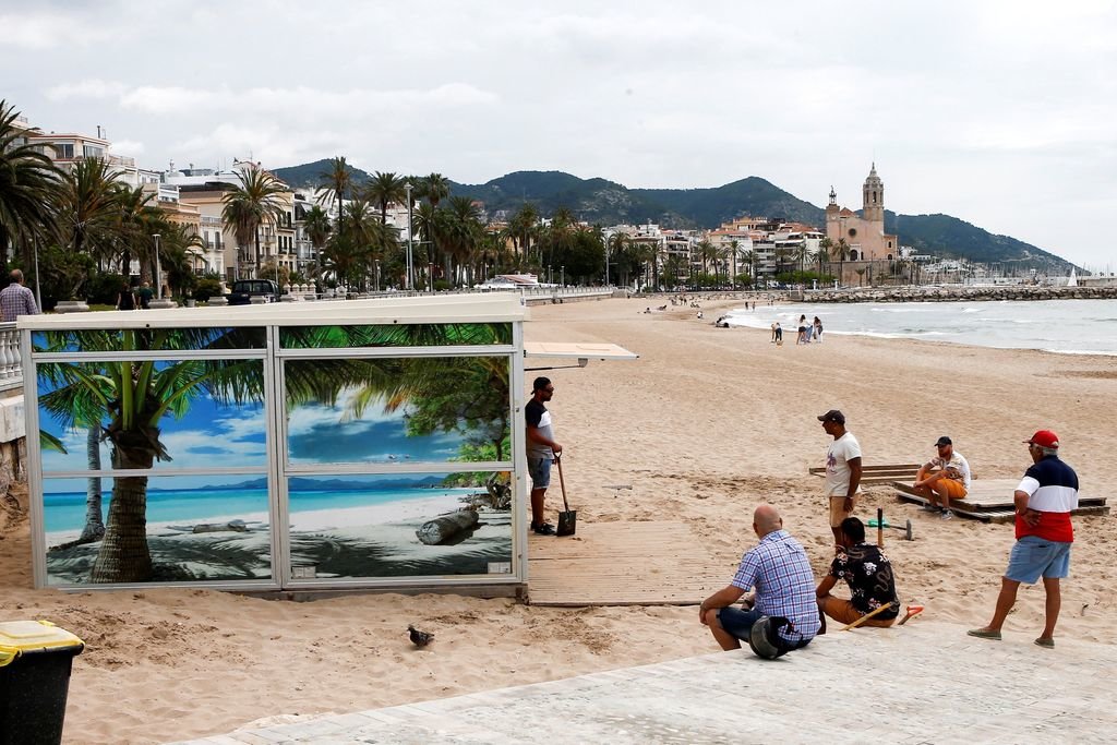 Varias personas preparan un chiringuito en la playa del paseo marítimo de Sitges.