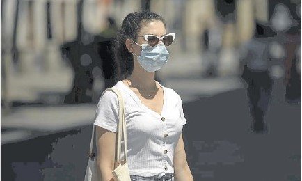 Una mujer con mascarilla sale a al calle protegiendo sus ojos con unas gafas de sol.