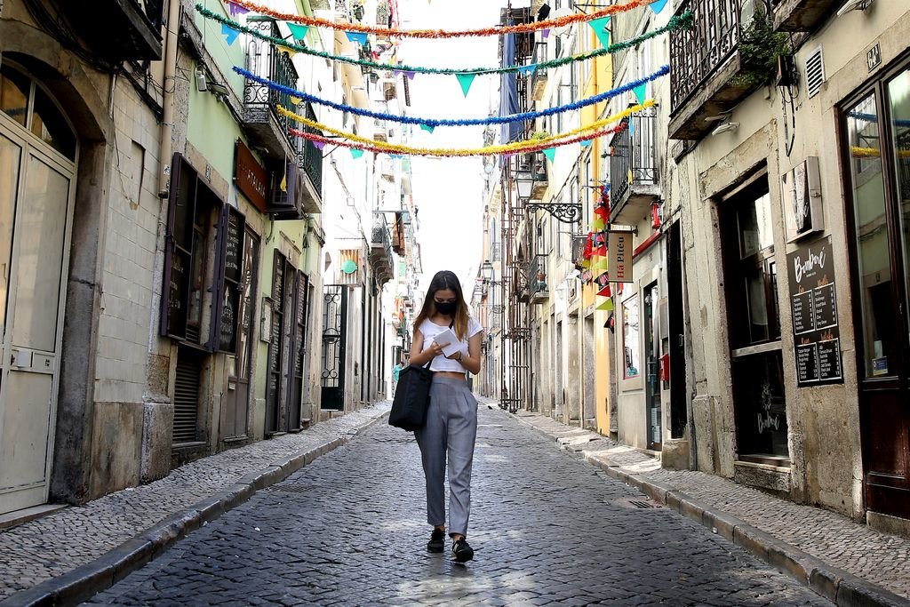 Una joven con mascarilla pasea por una calle del barrio antiguo de Lisboa.