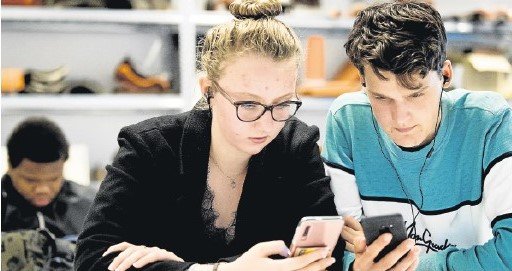 Dos jóvenes consultan sus respectivos teléfonos móviles.