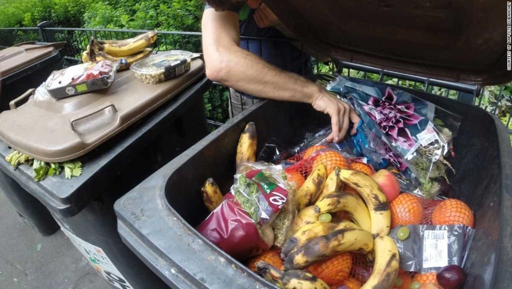 Una persona recoge comida desperdiciada de un contenedor de basura.