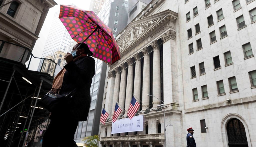 Una persona con mascarilla y paraguas pasa frente al edificio de la bolsa de Wall Street de Nueva York.