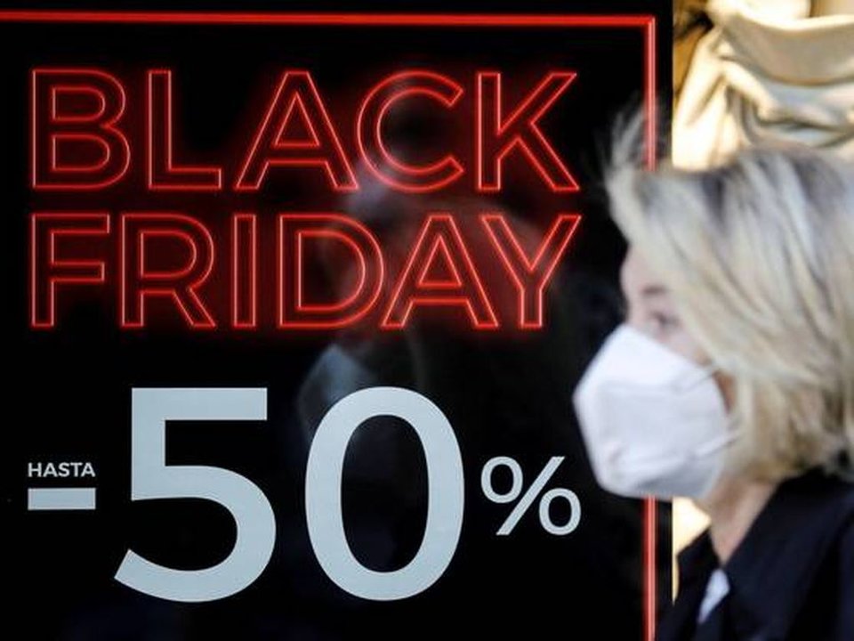 Una mujer con mascarilla pasea ante el escaparate de un comercio con promociones del "Black Friday".