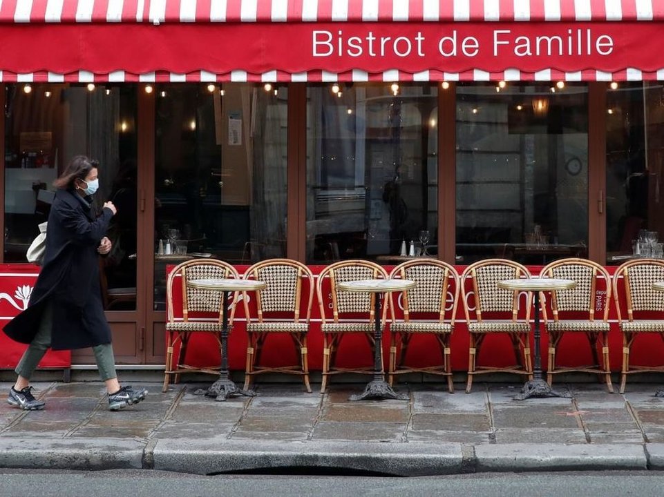 Una mujer con mascarilla pasa por delante de una terraza vacía en una calle de París.