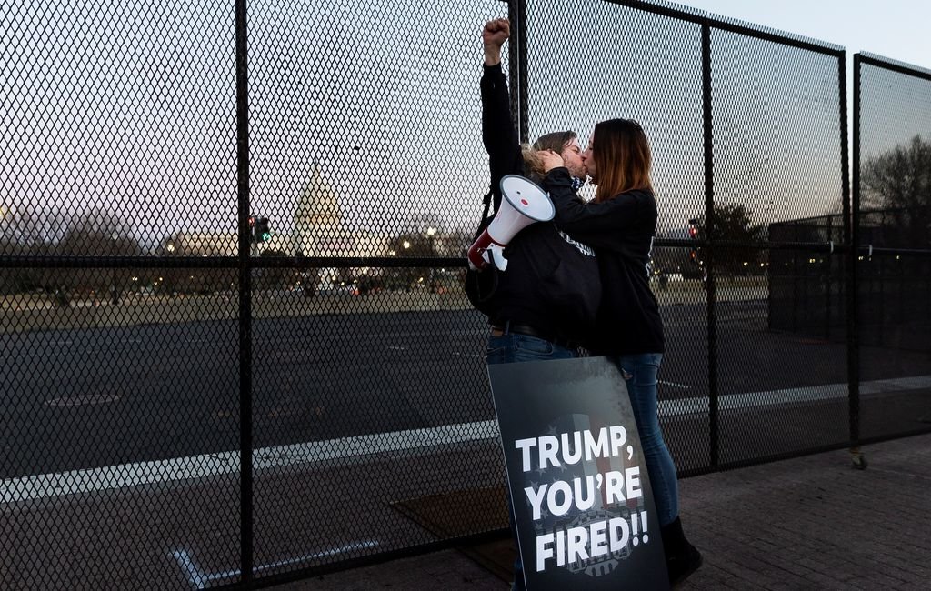 Una pareja se besa delante del Capitolio de EEUU, mientras sostiene una cartel que pone: ¡Trump estás despedido!.