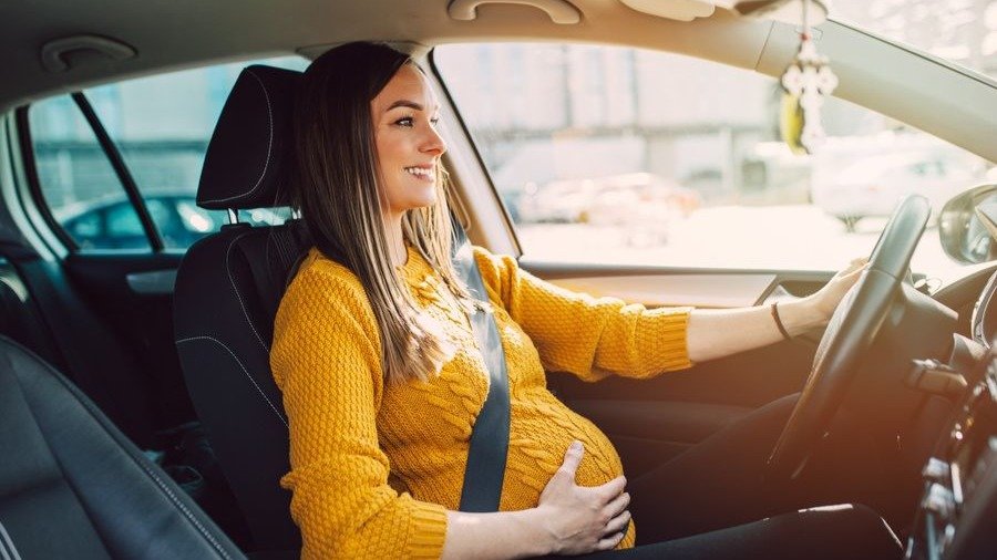 Una mujer conduca su vehículo con el cinturón de seguridad situado corractamente bajo el vientre.