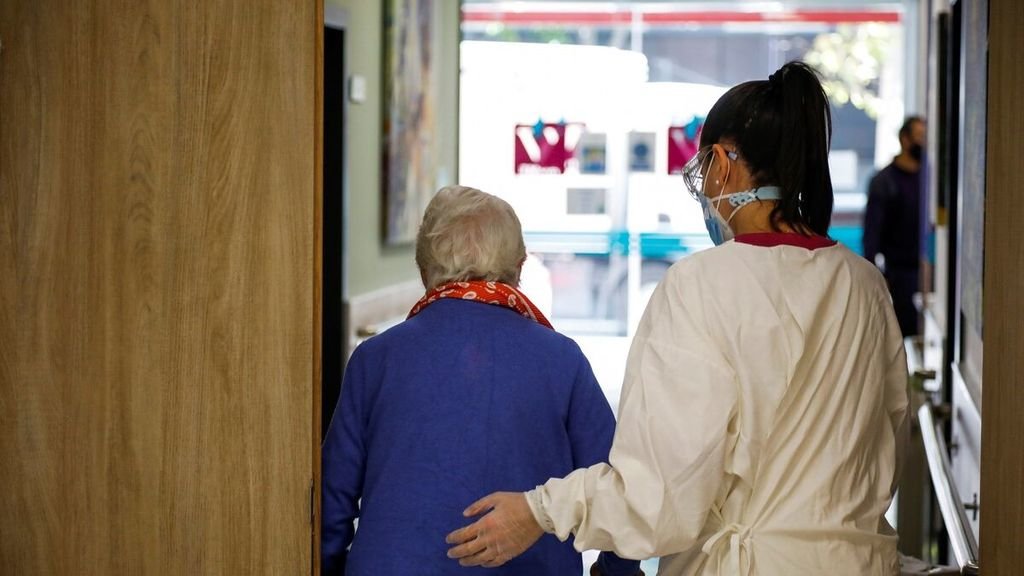 Una trabajadora sanitaria acompaña a una persona de avanzada edad hasta la puerta de la residencia.