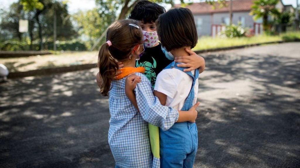 Tres escolares con mascarilla juegan en el patio de su colegio.