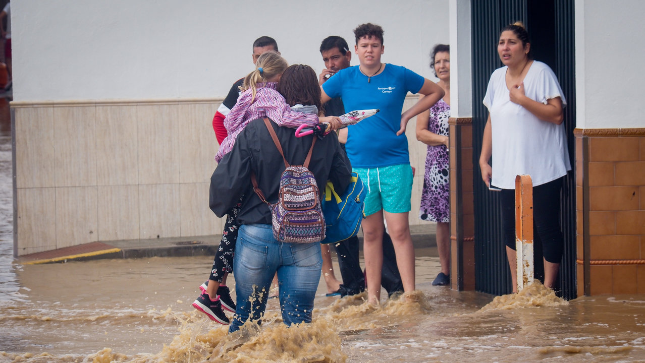 Una mujer con una niña en brazos cruza una calle inundada en Lepe.