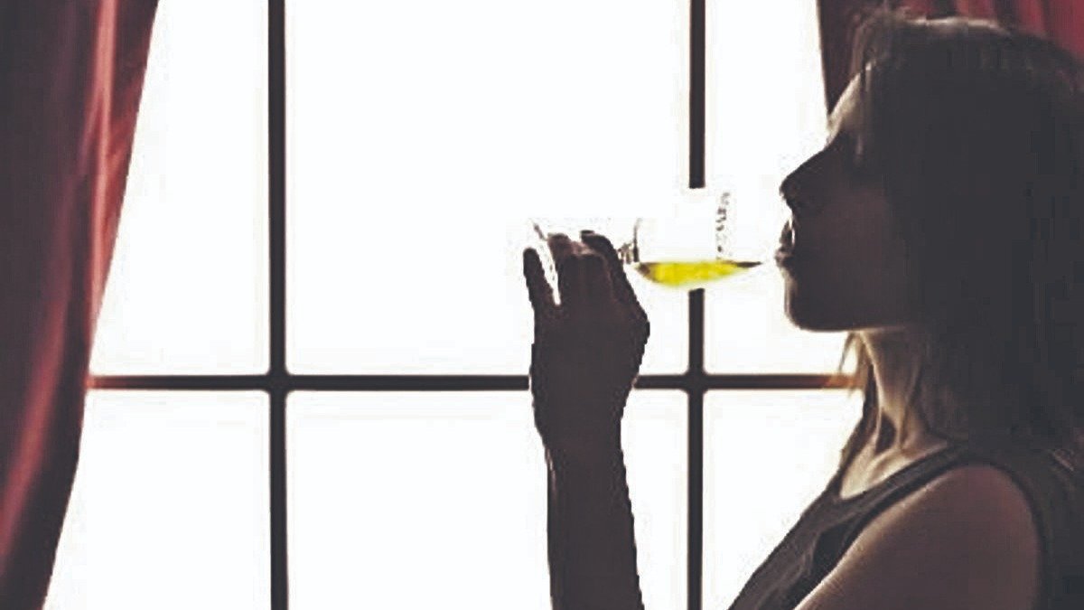 Una mujer bebe una copa de vino frente a una ventana.