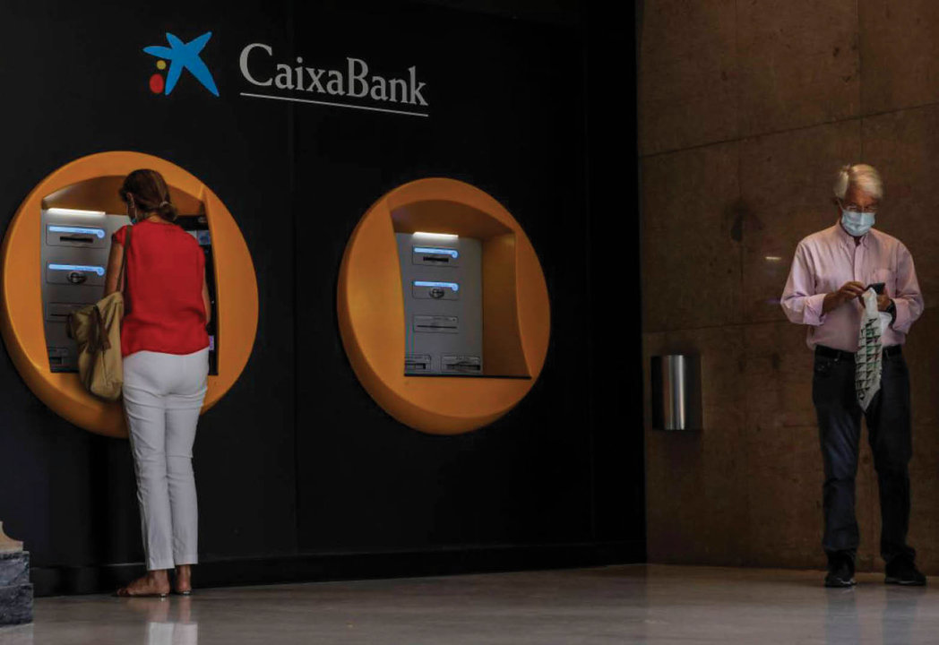 Dos clientes de CaixaBank sacando dinero en efectivo de cajeros de la entidad.