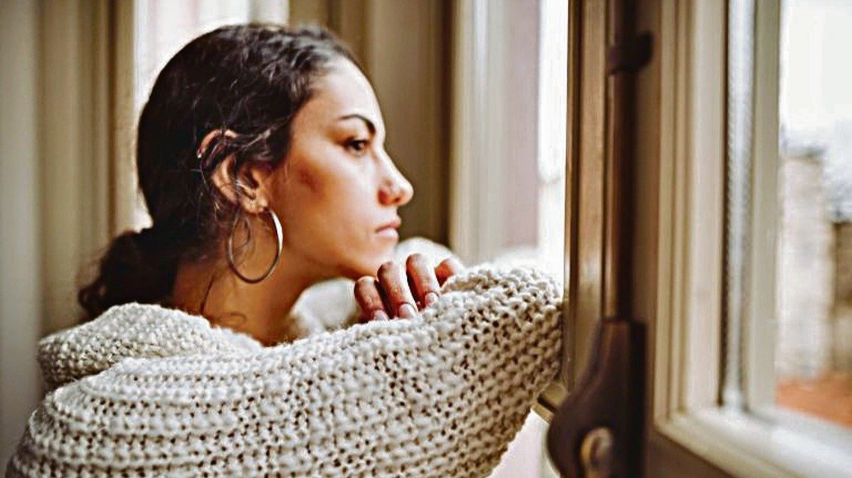 Una chica confinada en casa mirando a través de la ventana.