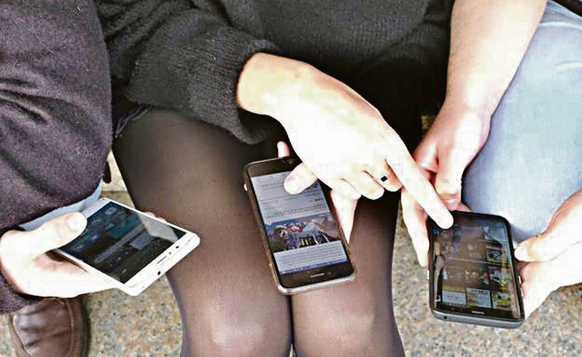 Tres adolescentes utilizan sus teléfonos móviles para acceder a redes sociales