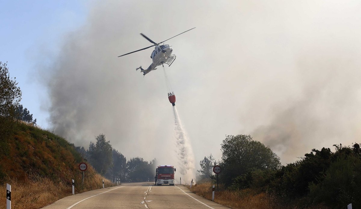 Uno de los helicópteros arroja agua ayer sobre el incendio de A Cañiza junto a la N-120, que permaneció cortada varias horas por el humo y el fuego.