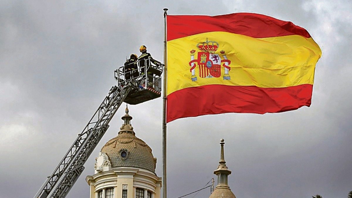 Dos bomberos reparan una bandera española en Alicante.