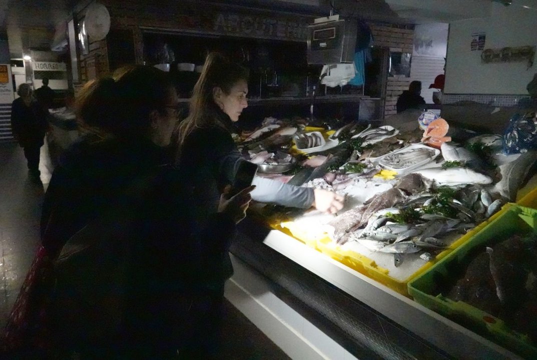Una clienta del mercado de As Travesas alumbra con su móvil a la vendedora de pescado para hacer la compra  durante el apagón.