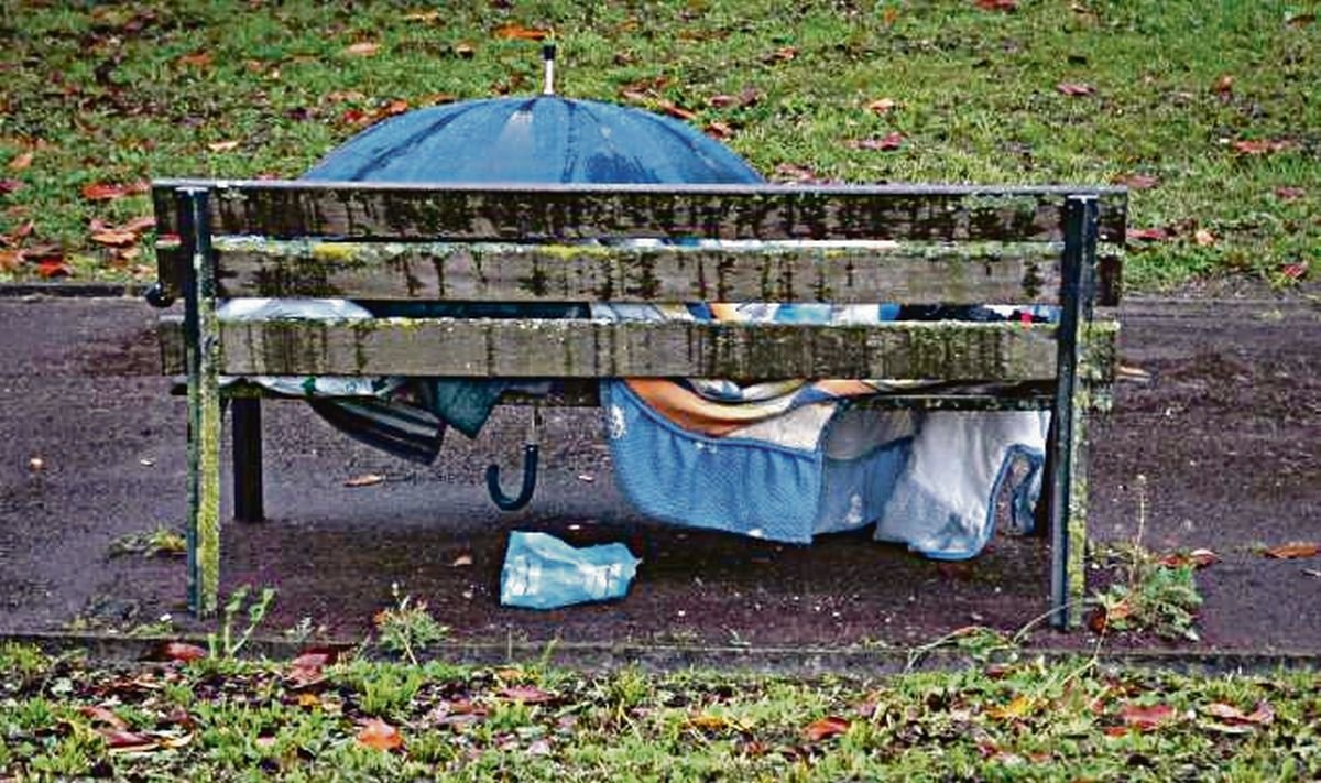 Un hombre sin hogar duerme en un banco bajo la lluvia.