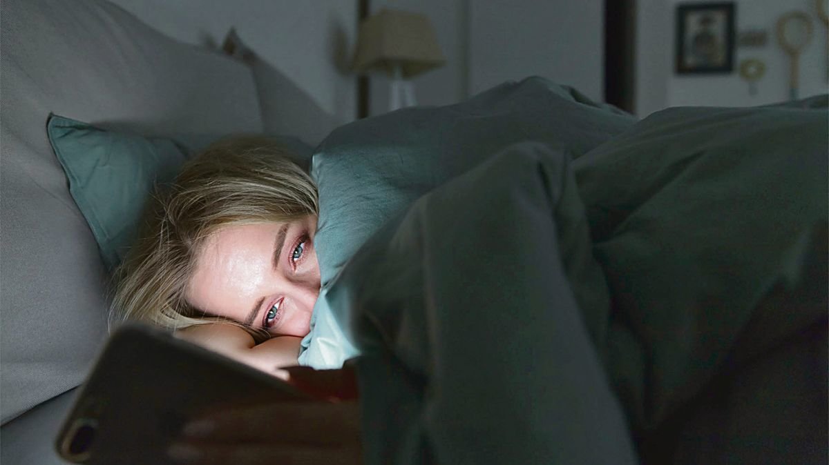 Una mujer observa su teléfono móvil en la cama antes de dormir.