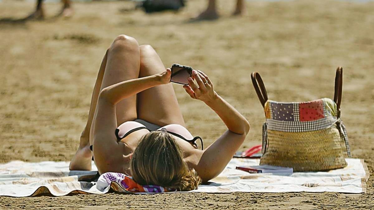 Una mujer consulta su teléfono móvil en una playa gallega.