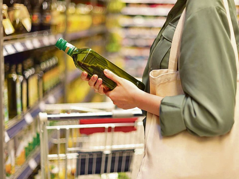 Una mujer decide la compra de una botella de aceite de oliva en un supermercado.