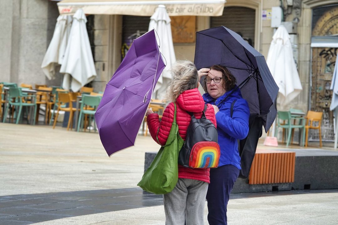 Dos mujeres intentan protegerse de la lluvia con sus paraguas.