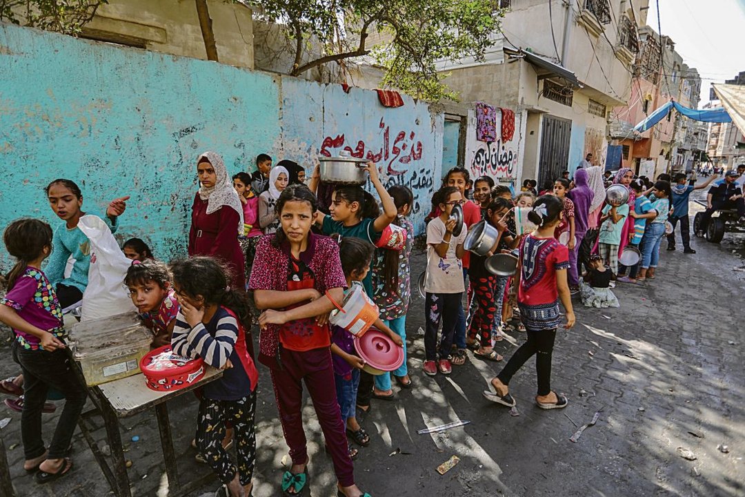 Grupo de palestinos desplazados en Rafah hacen cola para recibir comida caliente preparada.