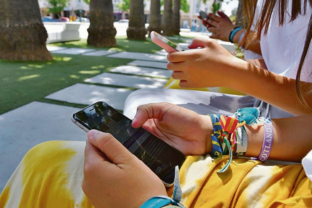 Un grupo de jóvenes observa sus teléfonos móviles en un parque.