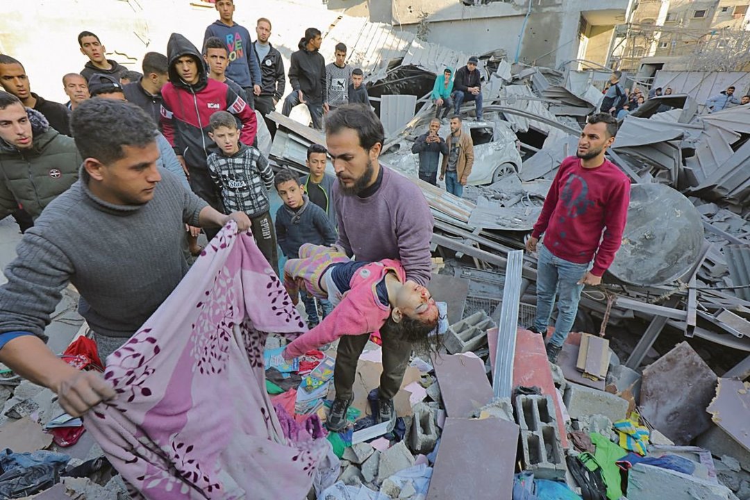 Un hombre carga a una niña herida tras un ataque a un edificio en el campamento de Nuseirat.