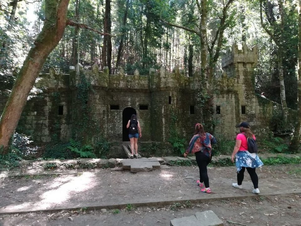Visitantes adentrándose en el castillo del Bosque Encantado de Aldán, un reclamo turístico muy potente en verano.