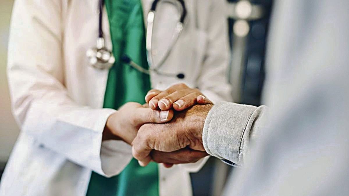 Un médico sostiene la mano de su paciente durante una consulta.