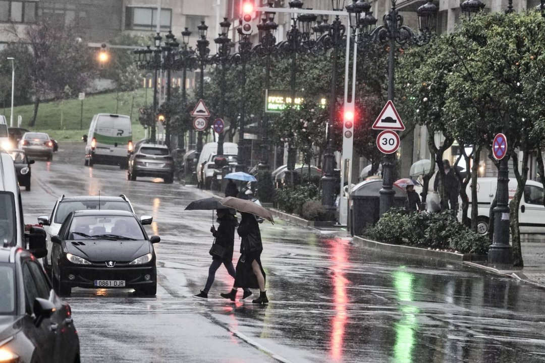 Dos mujeres cruzan un paso de peatones en Vigo bajo la lluvia con sus paraguas.