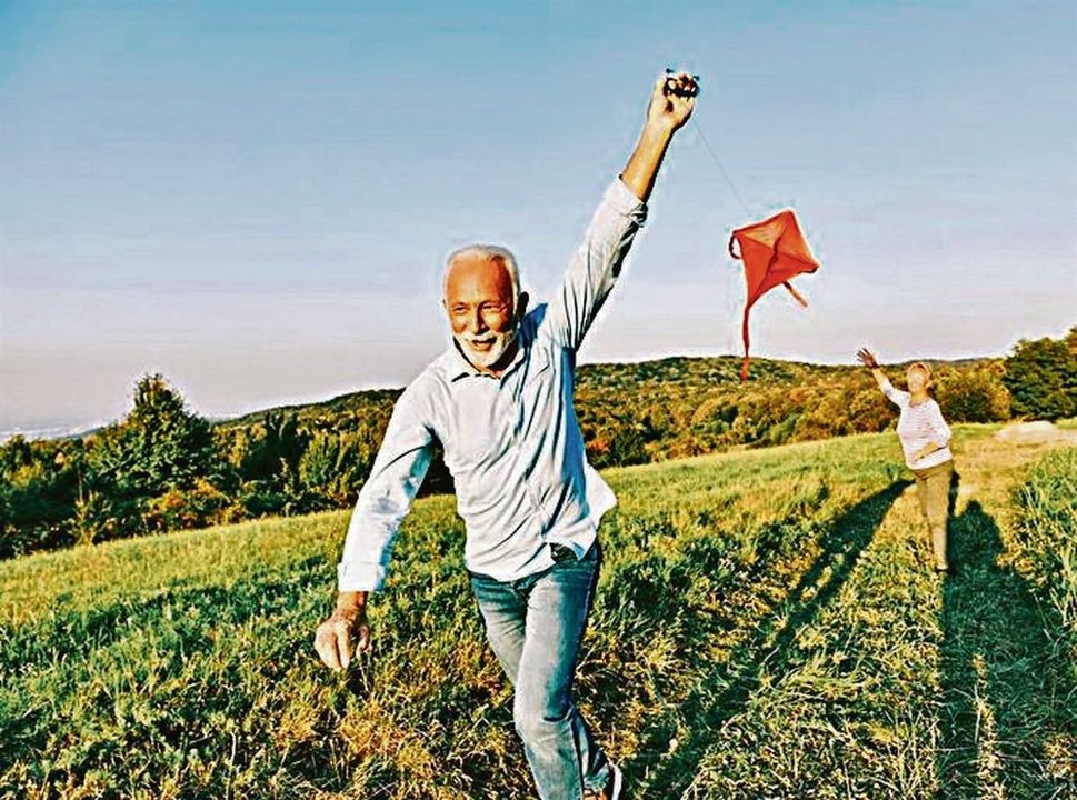 Una pareja de personas mayores juegan felices con una cometa.
